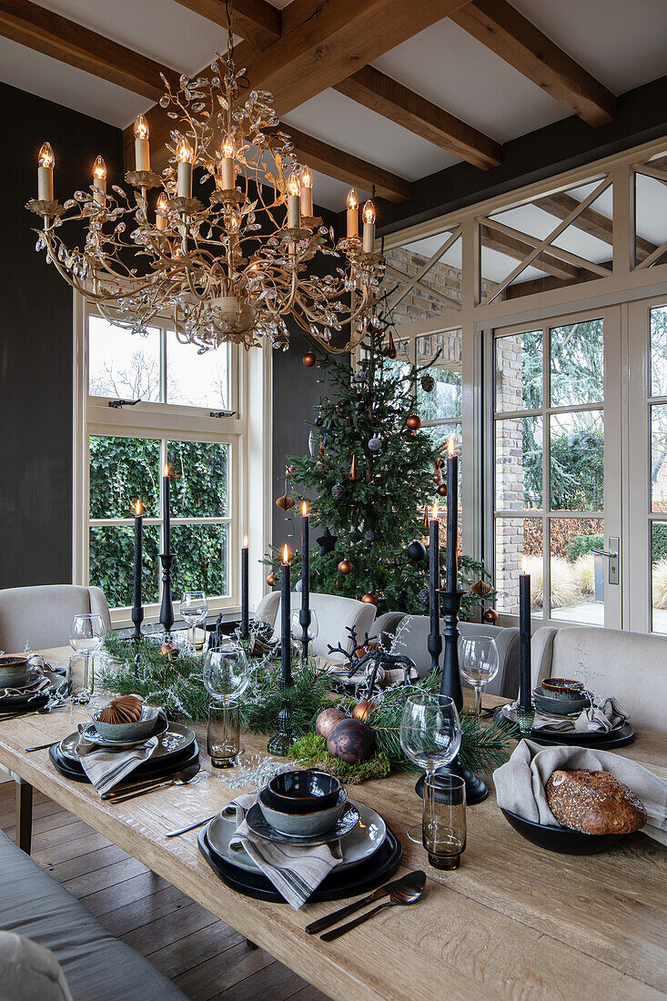 Dining table set for Christmas with chandelier, black candles and Christmas tree in the background