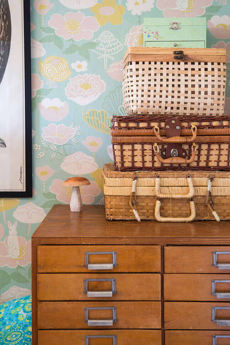 Chest of drawers with woven baskets in front of floral patterned wallpaper