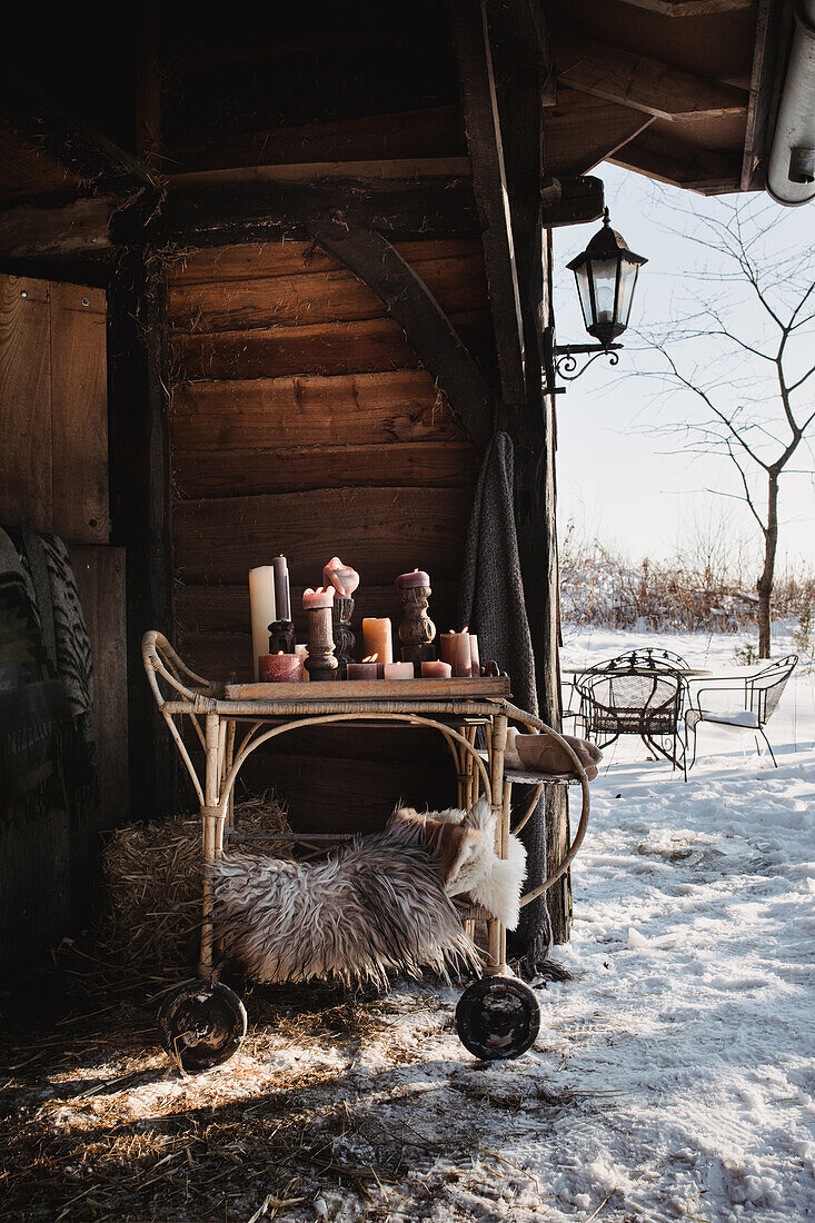 Rattan serving trolley with candles under wooden roof, snowy surroundings