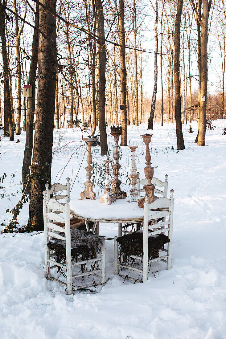 Weißer Gartentisch mit Kerzenständern im verschneiten Wald