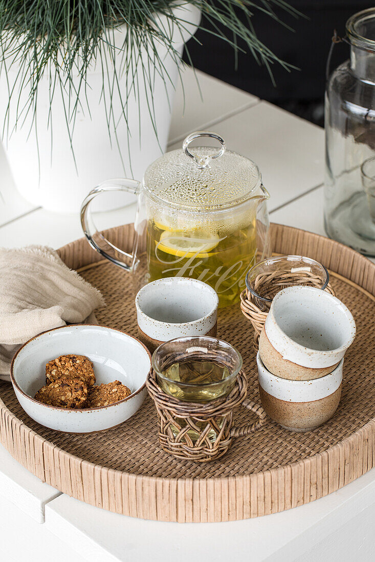 Glass teapot, biscuits and ceramic cups on tray