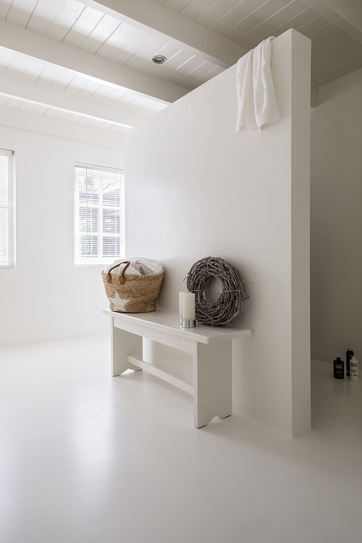 White, minimalist bathroom with bench, basket and decorative wreath