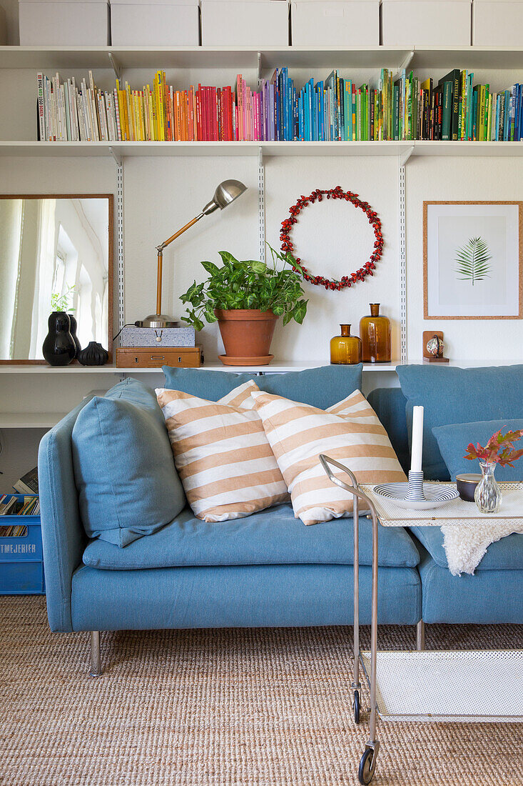 Blue sofa with striped cushions in front of a shelf with books in assorted colours