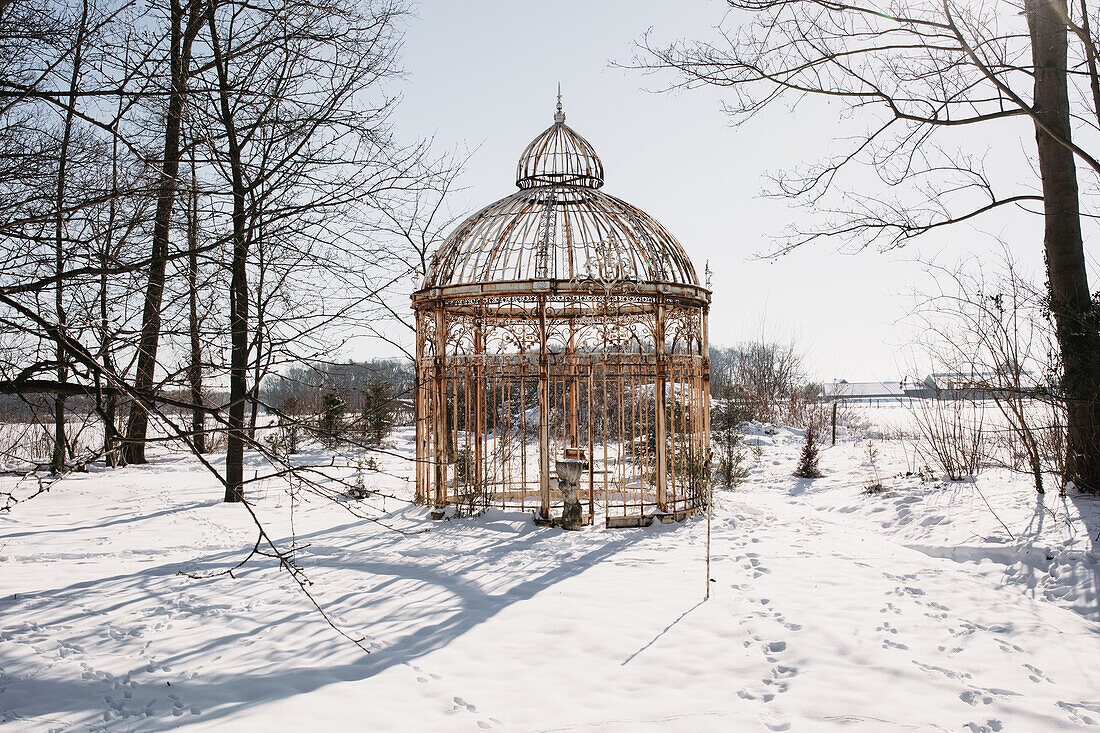 Vintage pavilion in a snowy winter garden with bare trees