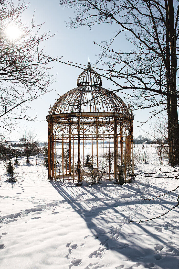 Antique, wrought-iron pavilion in a garden covered in snow