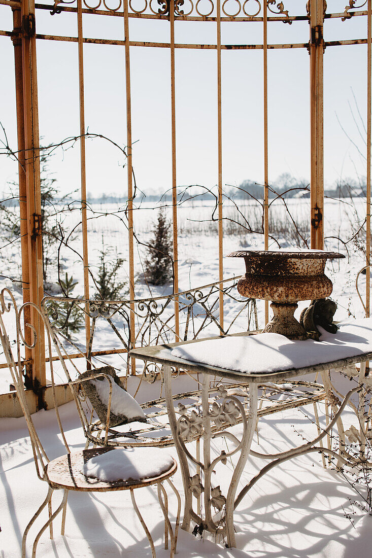 Snow-covered, antique garden table with chair and bench in the conservatory