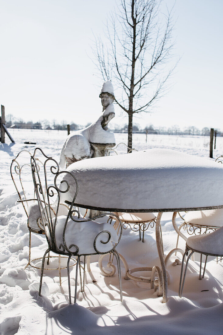 Snow-covered garden table with chairs in winter garden