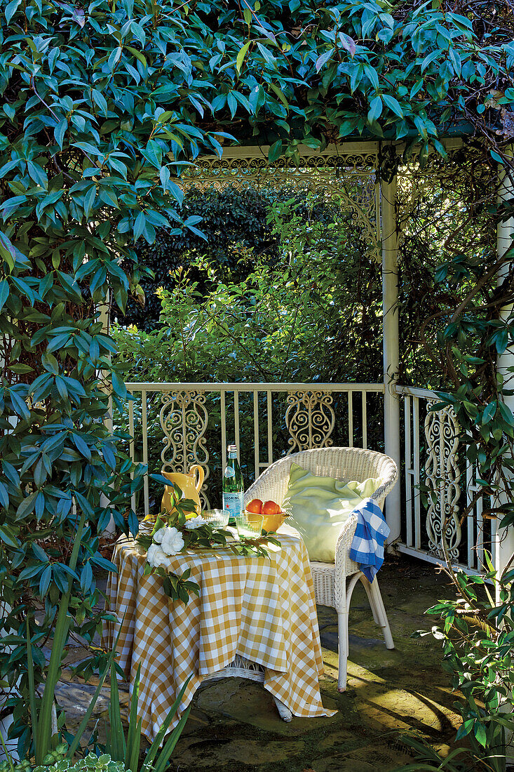 Weißer Rattanstuhl und gedeckter Tisch in von Pflanzen überwachsener Pergola im Garten