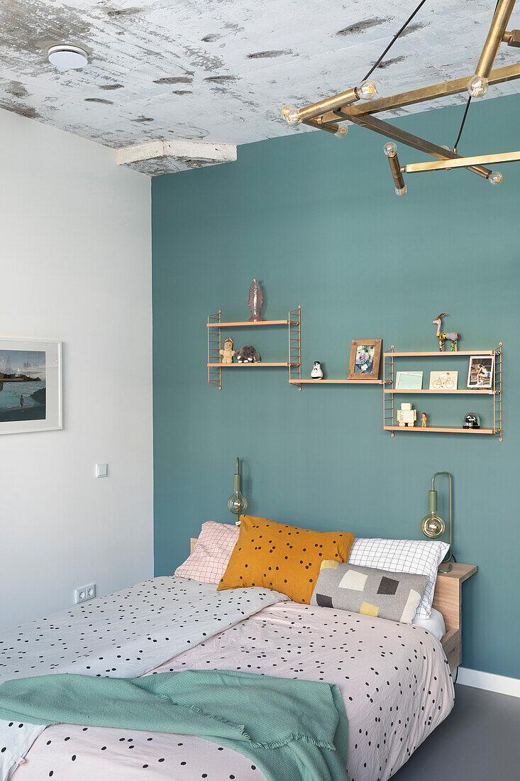 Modern bedroom with green-blue accent wall, shelves and brass ceiling light