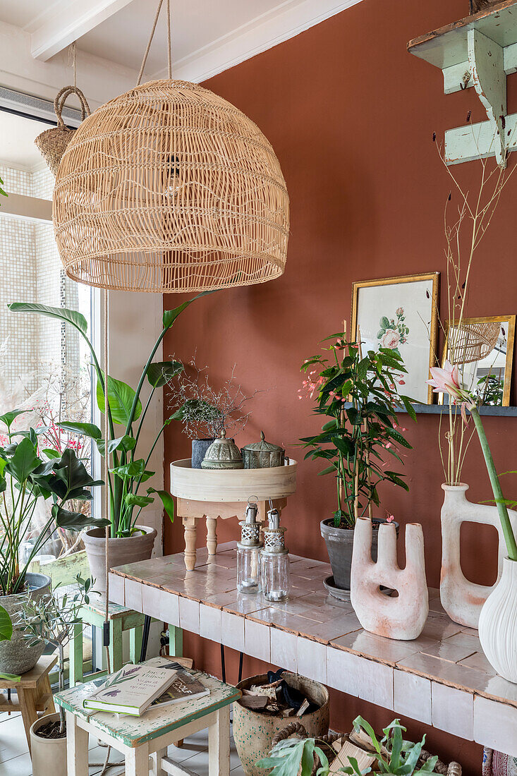 Corner with lots of plants and vases on a tiled table, wall in rust red