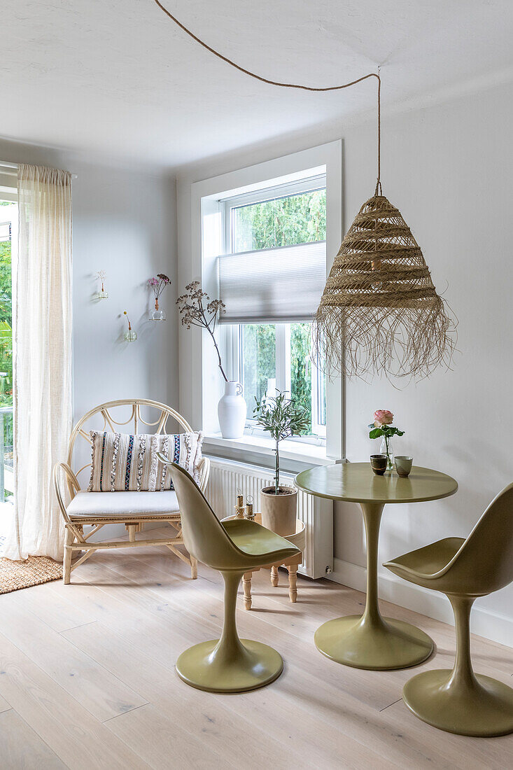 Dining area with olive-colored table and tulip chairs, armchair and rattan ceiling lamp