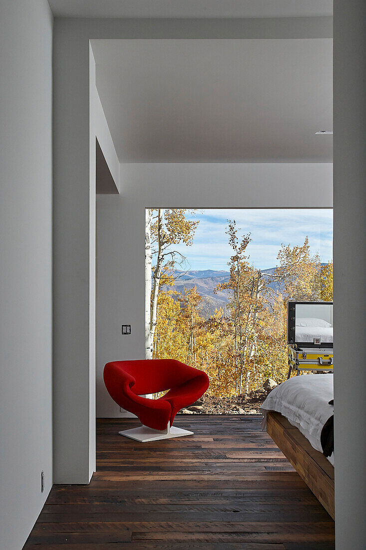 View into the guest room with floor-to-ceiling glass wall and red chair