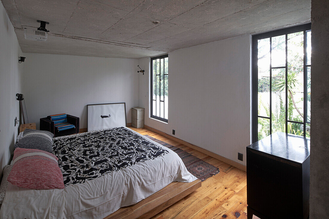 Schlafzimmer mit Doppelbett, Holzdielenboden, Fenster mit Metallgitter und Betondecke