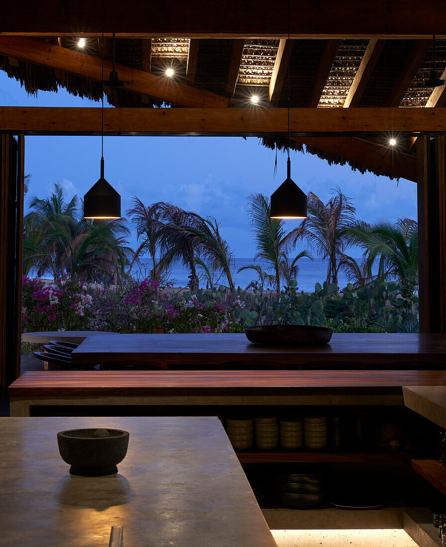 Essbereich mit Holzelementen im Strandhaus mit Blick auf das Meer in der Abenddämmerung