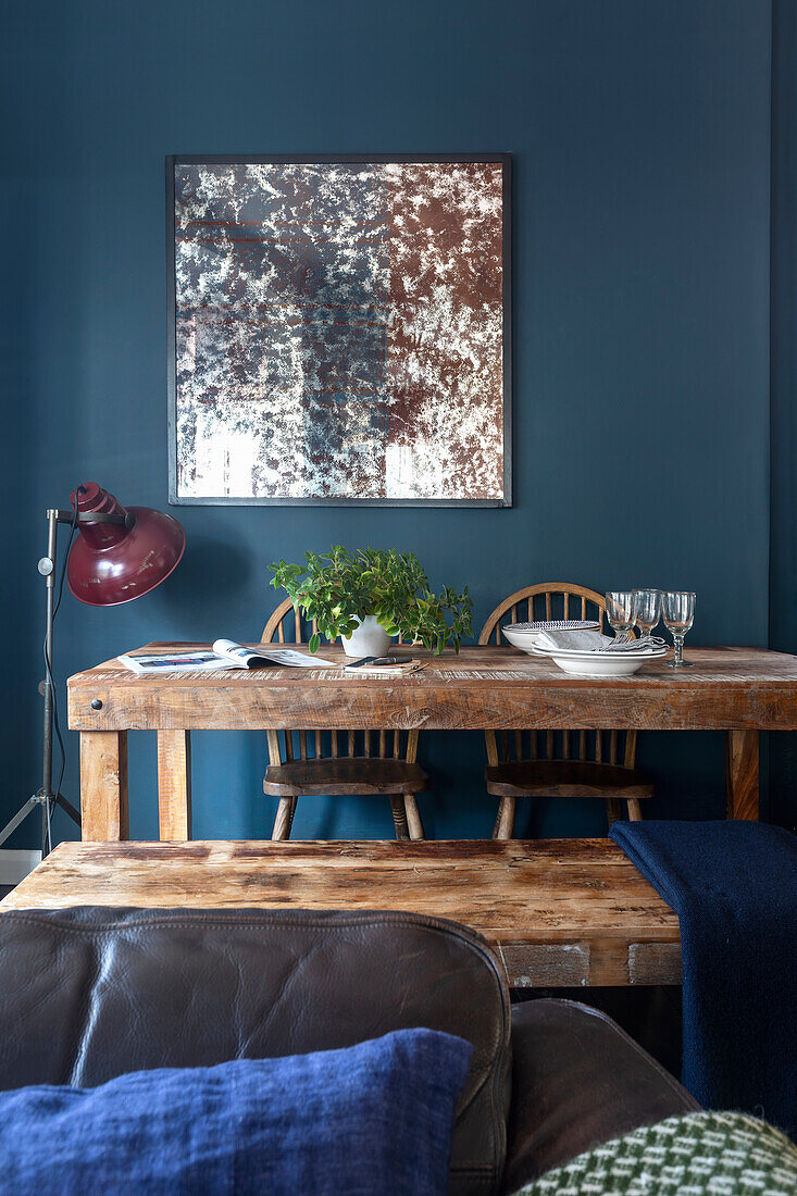 Wooden dining table in front of blue painted wall with picture