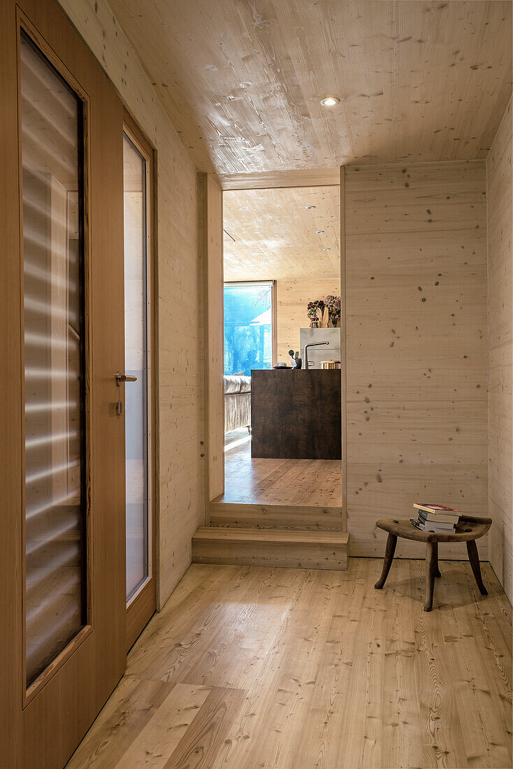 Wood-paneled hallway with glass door and small wooden stool, view of the kitchen