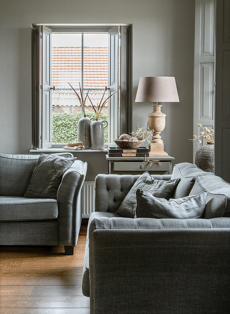 Gemütliche Sitzecke mit grauen Sofas, Beistelltisch und Tischlampe vor Fenster