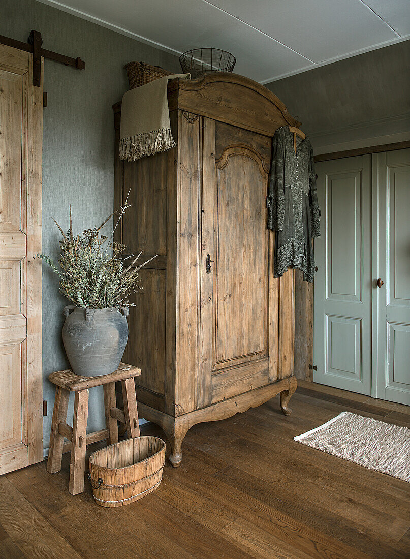 Alter Holzschrank im Schlafzimmer mit rustikalen Dekorationen und Strauß aus Trockenblumen und -gräsern