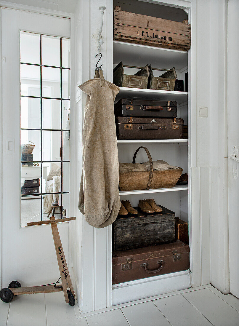 Regal mit rustikalen Holzkisten, Vintage-Koffern und Holz-Roller in weißem Flur