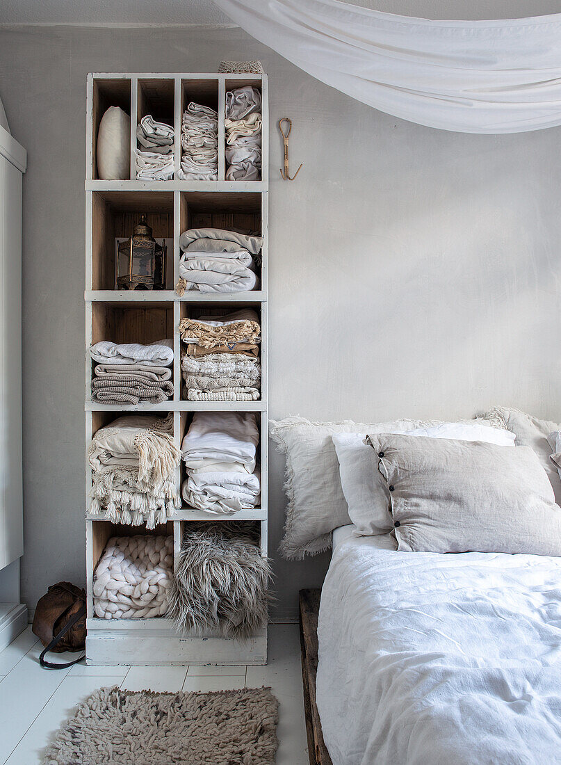 Bedroom with wall shelf filled with folded bed linen and blankets