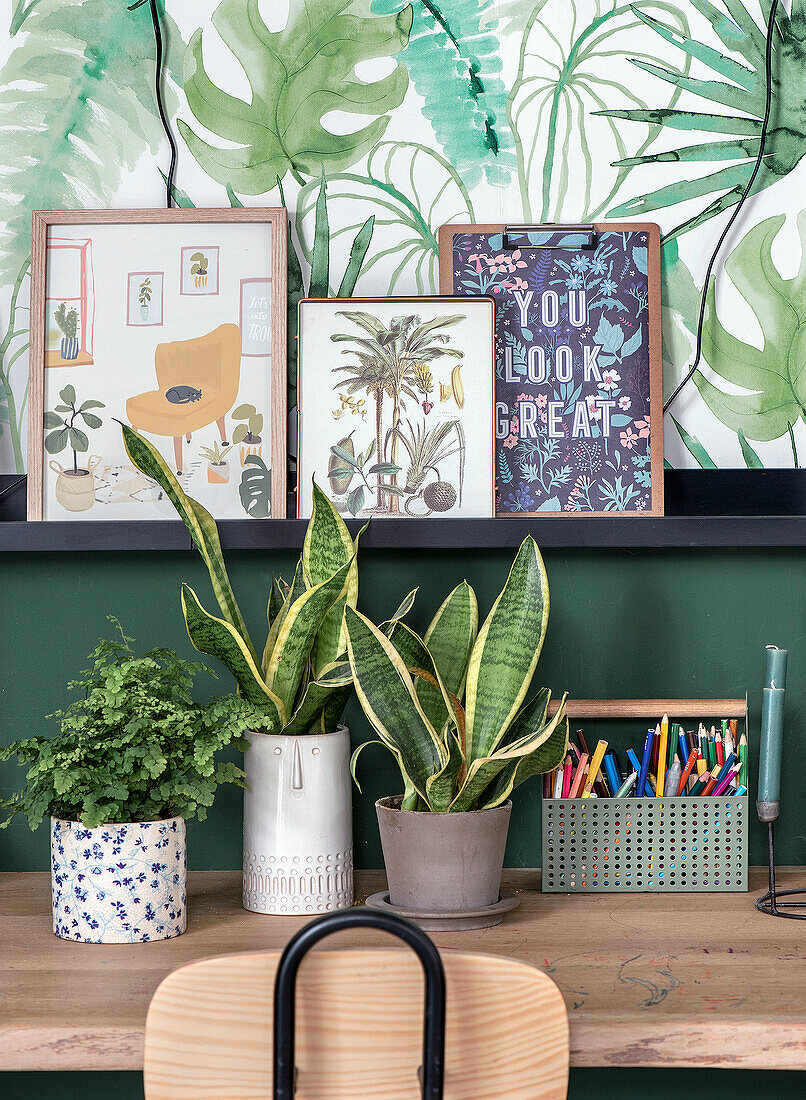 Desk with plants and framed art in front of botanical wallpaper