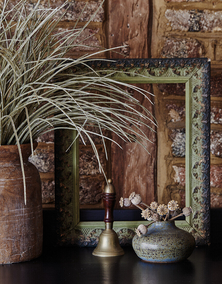 Decorative still life with dried flowers, vase and picture frame in front of brick wall