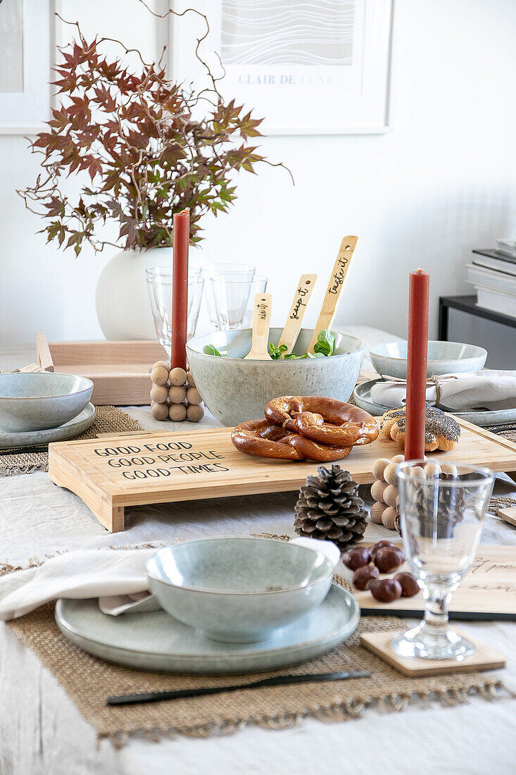 Herbstlich gedeckter Esstisch mit Holzbrett, Brezeln und roten Kerzen