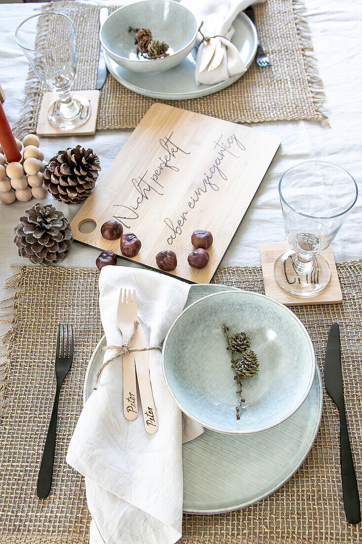 Rustic table setting with pine cones and wooden board with lettering