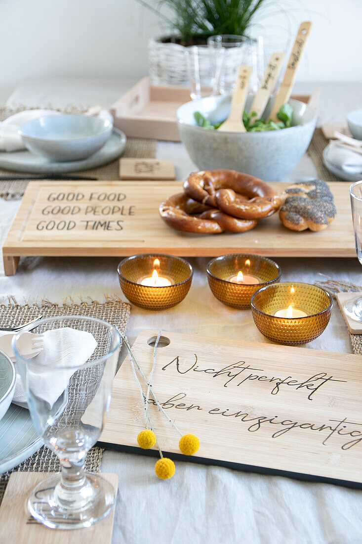 Gedeckter Tisch mit Brezen, Kerzenschalen und personalisierten Holzbrettern