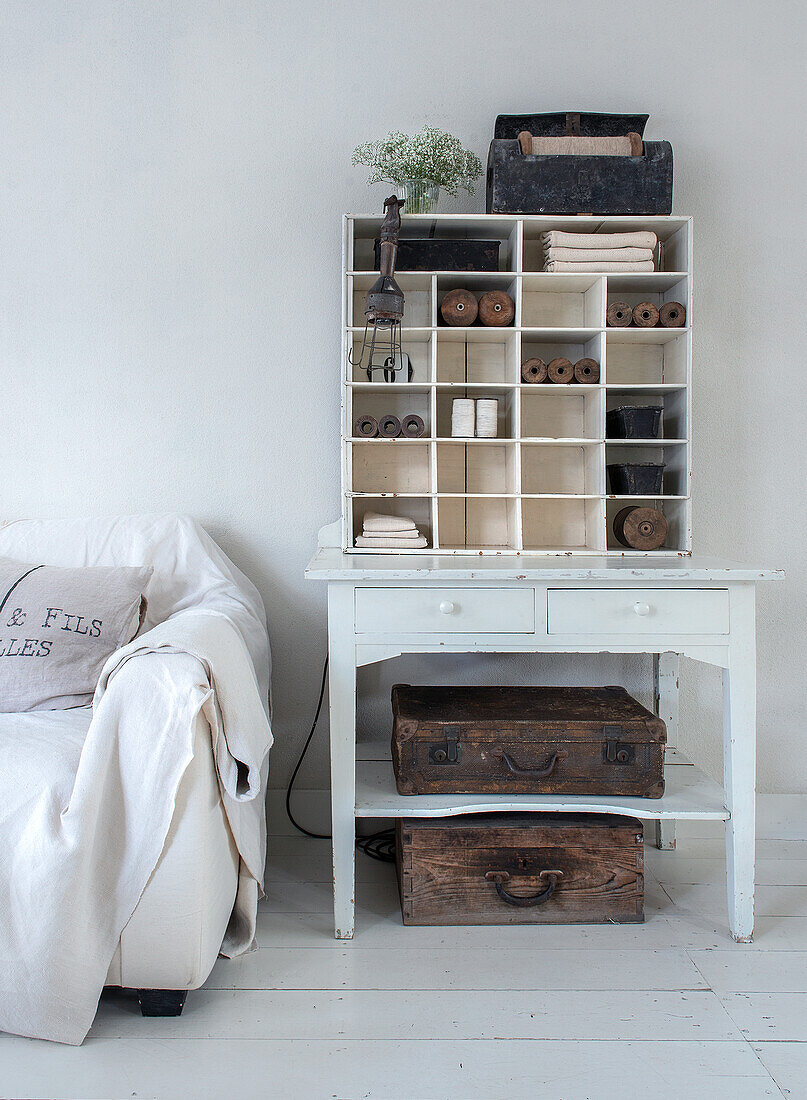 White storage shelf with spools of thread and old wooden boxes next to white sofa