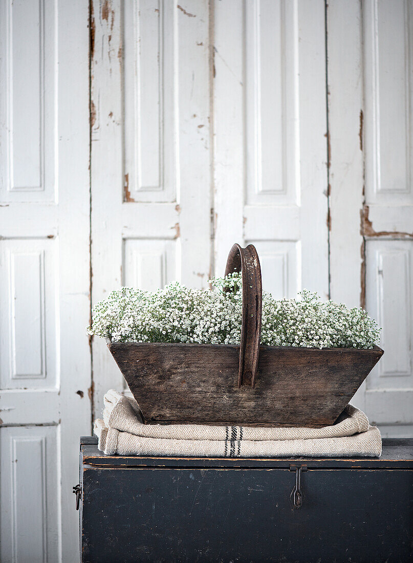 Wooden basket with baby's breath on linen cloth in front of wooden door