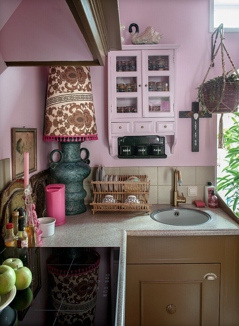 Compact kitchen with brown and pink accents, spice rack and antique table lamp