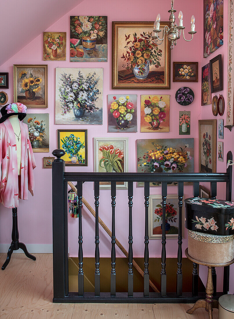 Staircase with black banister, pink wall and numerous flower pictures