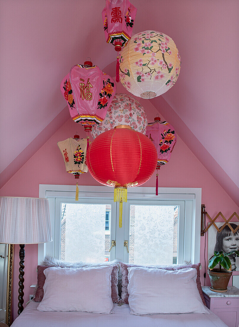 Decorative cardboard lanterns above a bed with pink wall paint in the bedroom