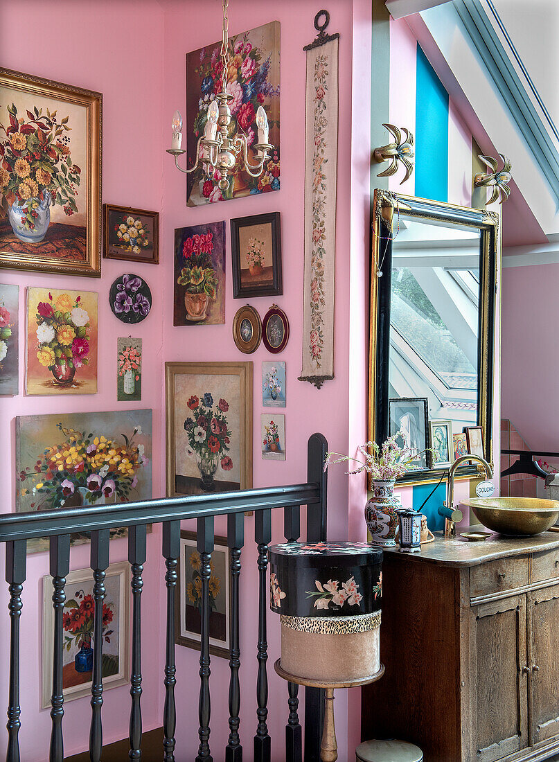 Staircase with flower paintings and vintage wooden chest of drawers in front of a pink wall