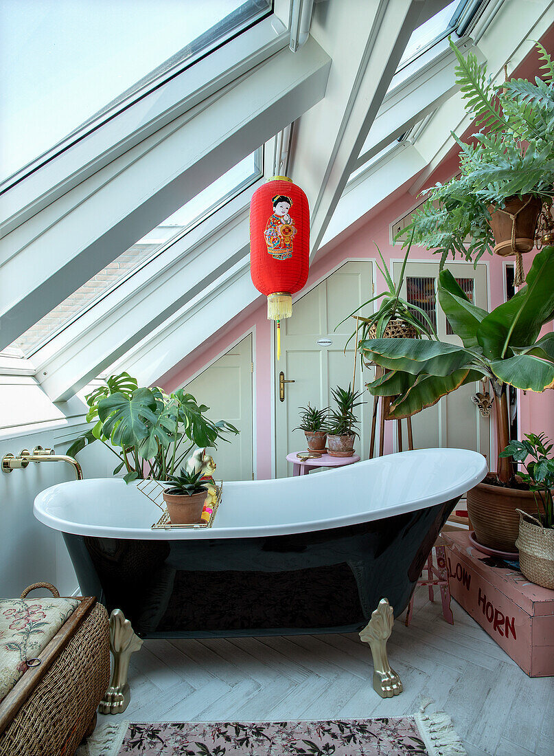 Freestanding vintage bathtub under sloping roof with plants and Asian lantern