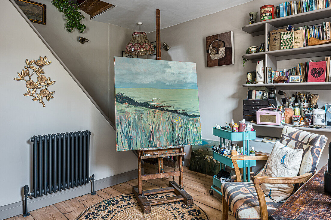 Artist's studio with easel, paintings and shelves full of painting utensils