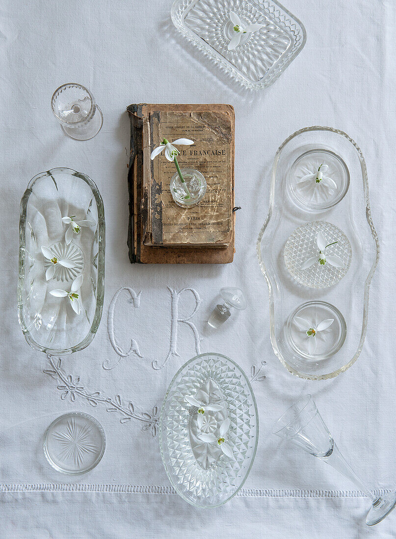 Vintage-Glasgeschirr und altes Buch auf bestickter Leinentischdecke