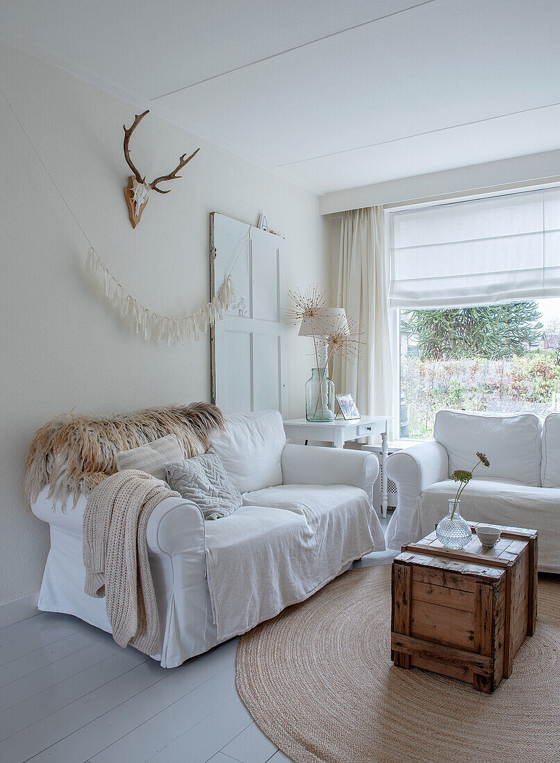 Bright living room with white sofas, wooden chest and antler wall decoration