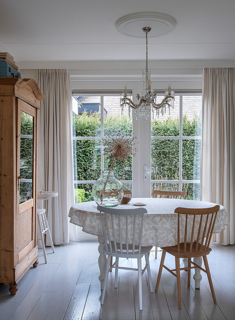 Dining room with round table, wooden furniture and chandelier in front of large windows