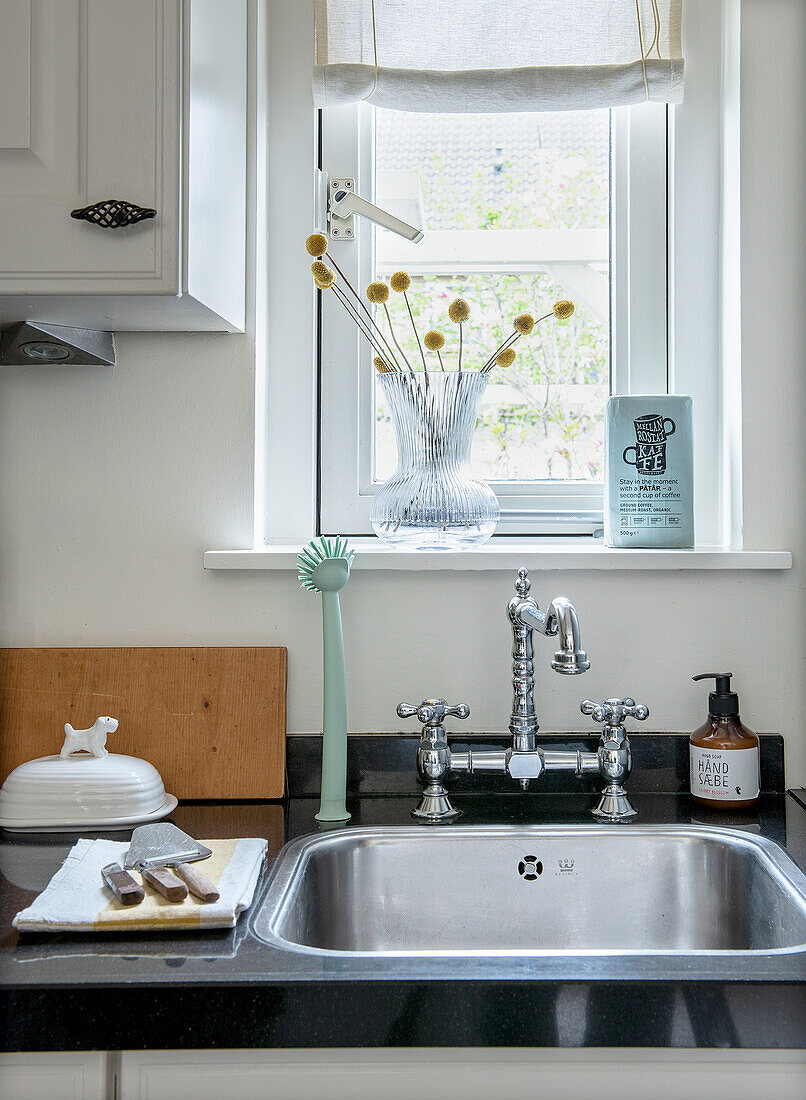 Kitchen unit with stainless steel sink, nostalgic taps and glass vase in front of window