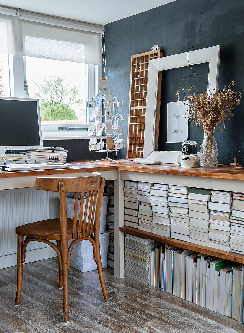 Arbeitszimmer mit Holzstuhl, Bücherstapeln und schwarzer Akzentwand