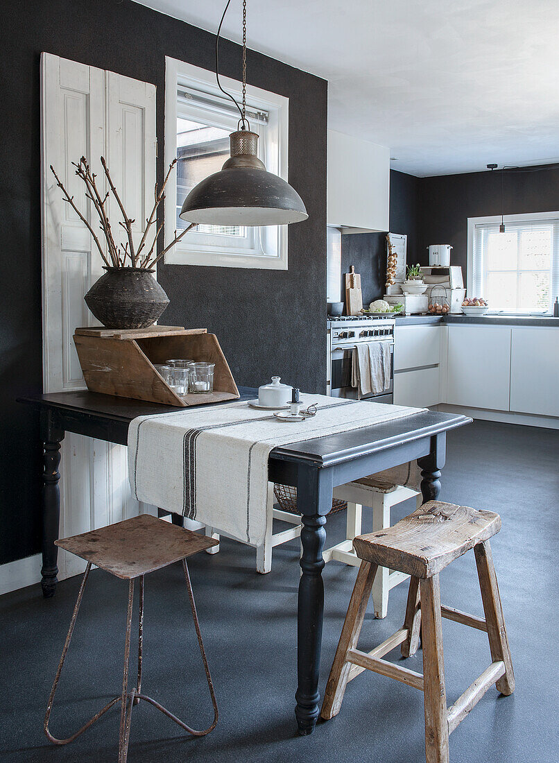 Open-plan dining area with black wooden table, rustic stools and hanging metal lamp