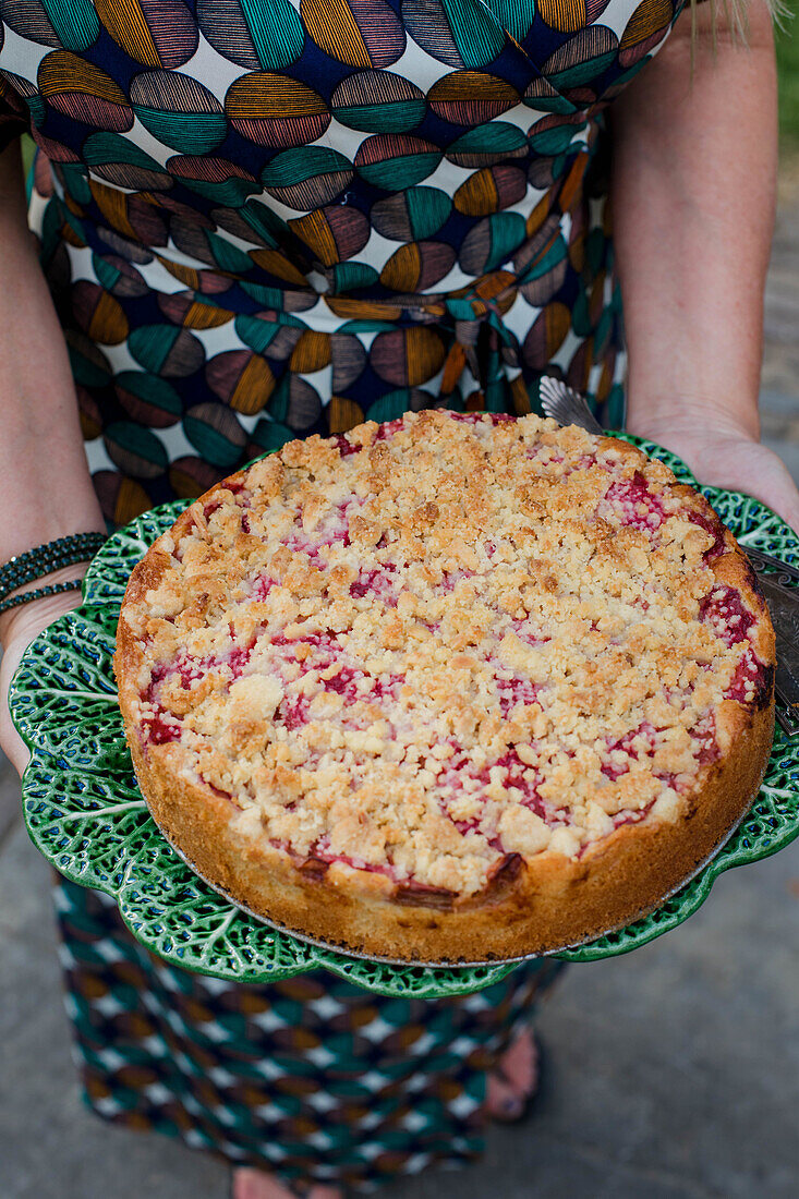 Frau hält Obst-Streuselkuchen auf grün gemustertem Keramikteller