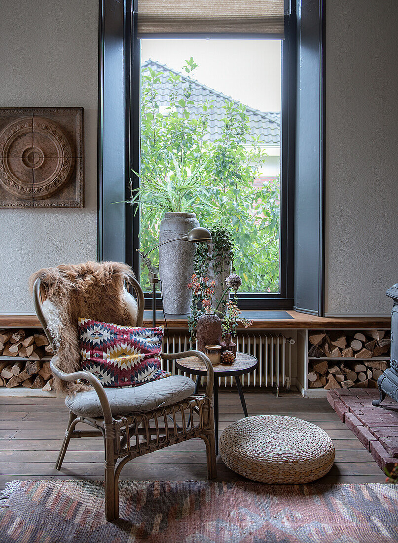 Rattansessel und Holzhocker in rustikalem Wohnzimmer mit großem Fenster