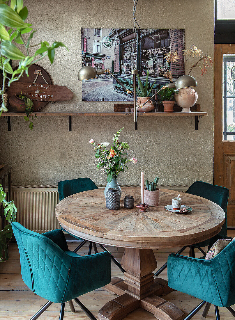 Round wooden table with green velvet chairs and bouquet of flowers in the dining room