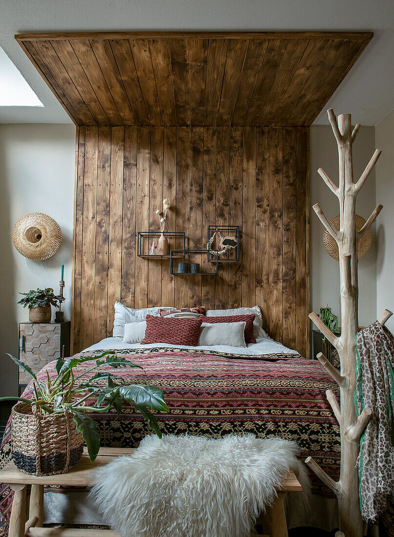 Schlafzimmer mit Holzvertäfelung und gemustertem Bettüberwurf im Ethno-Stil