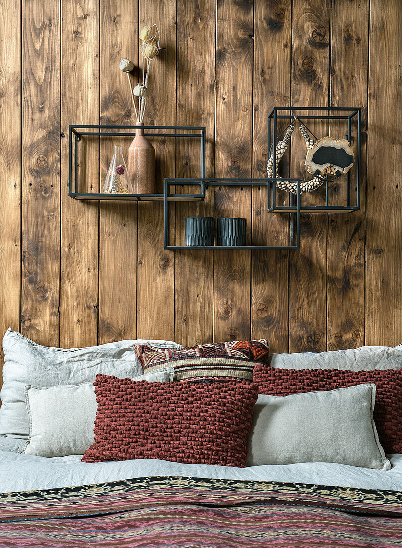 Bed with cushions and metal wall shelves on a wooden wall