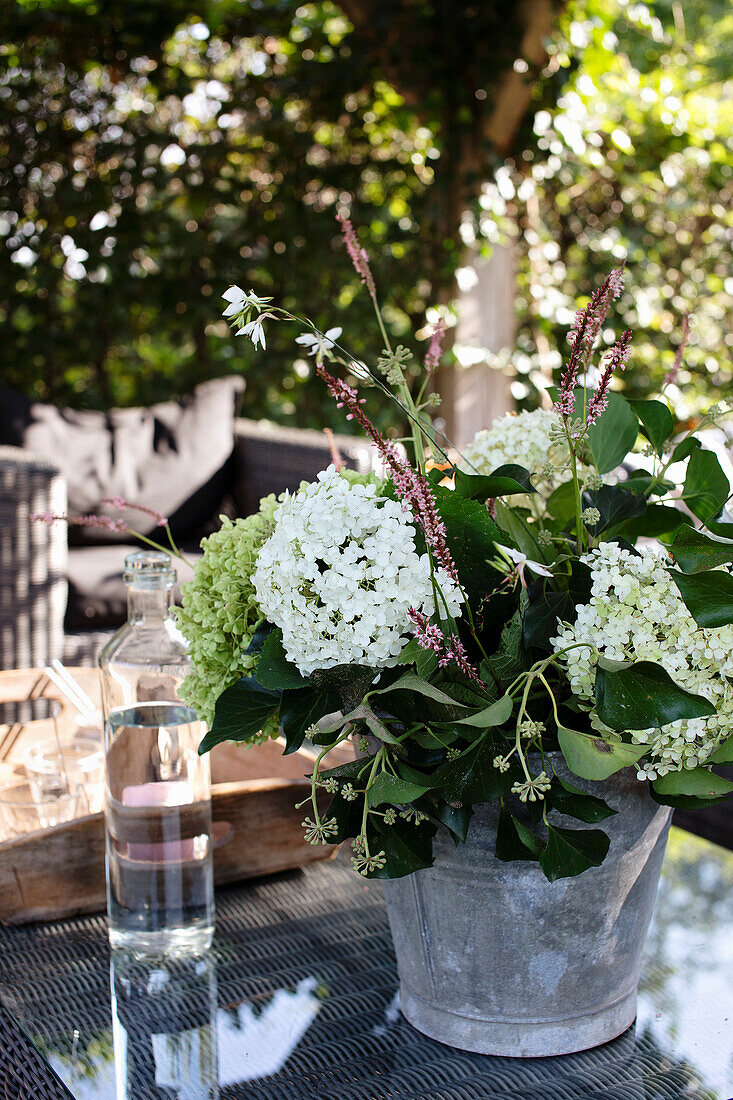 Zinkeimer mit weißen Hortensien (Hydrangea) auf Gartentisch