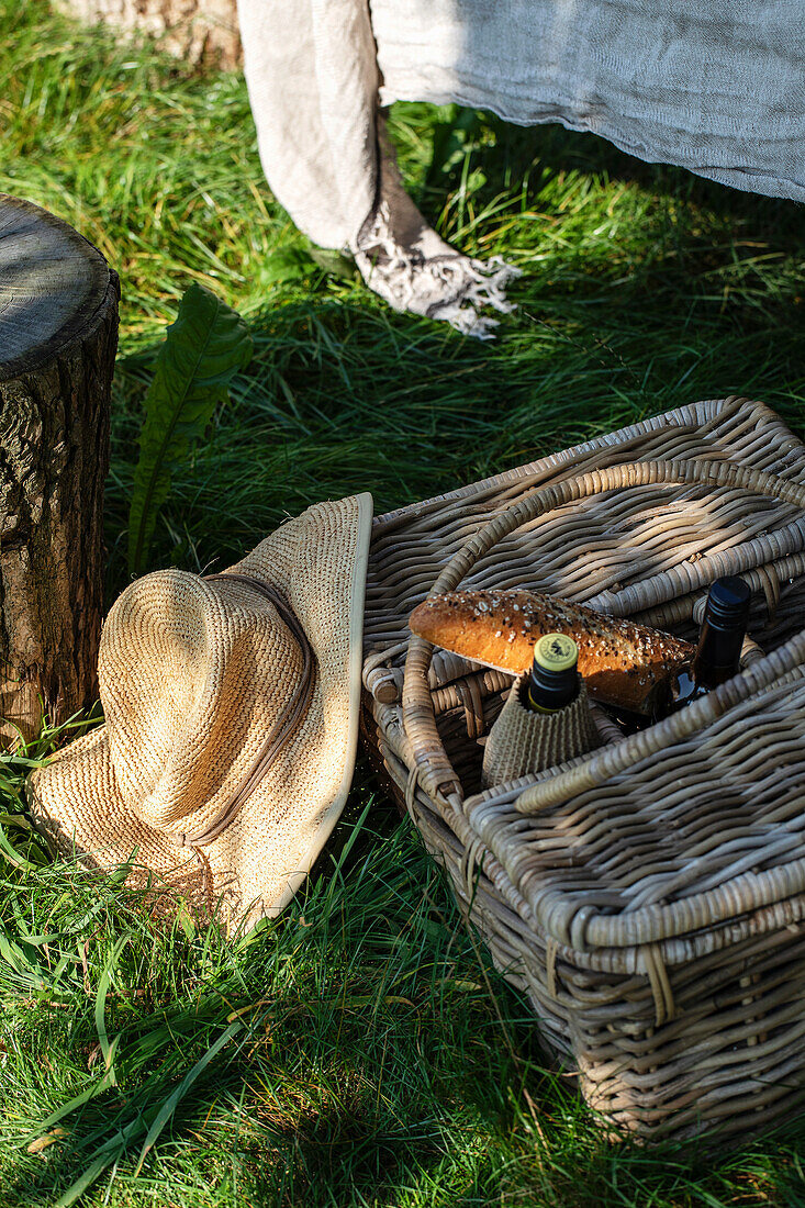 Picnic basket and straw hat in the sunny garden on a green lawn